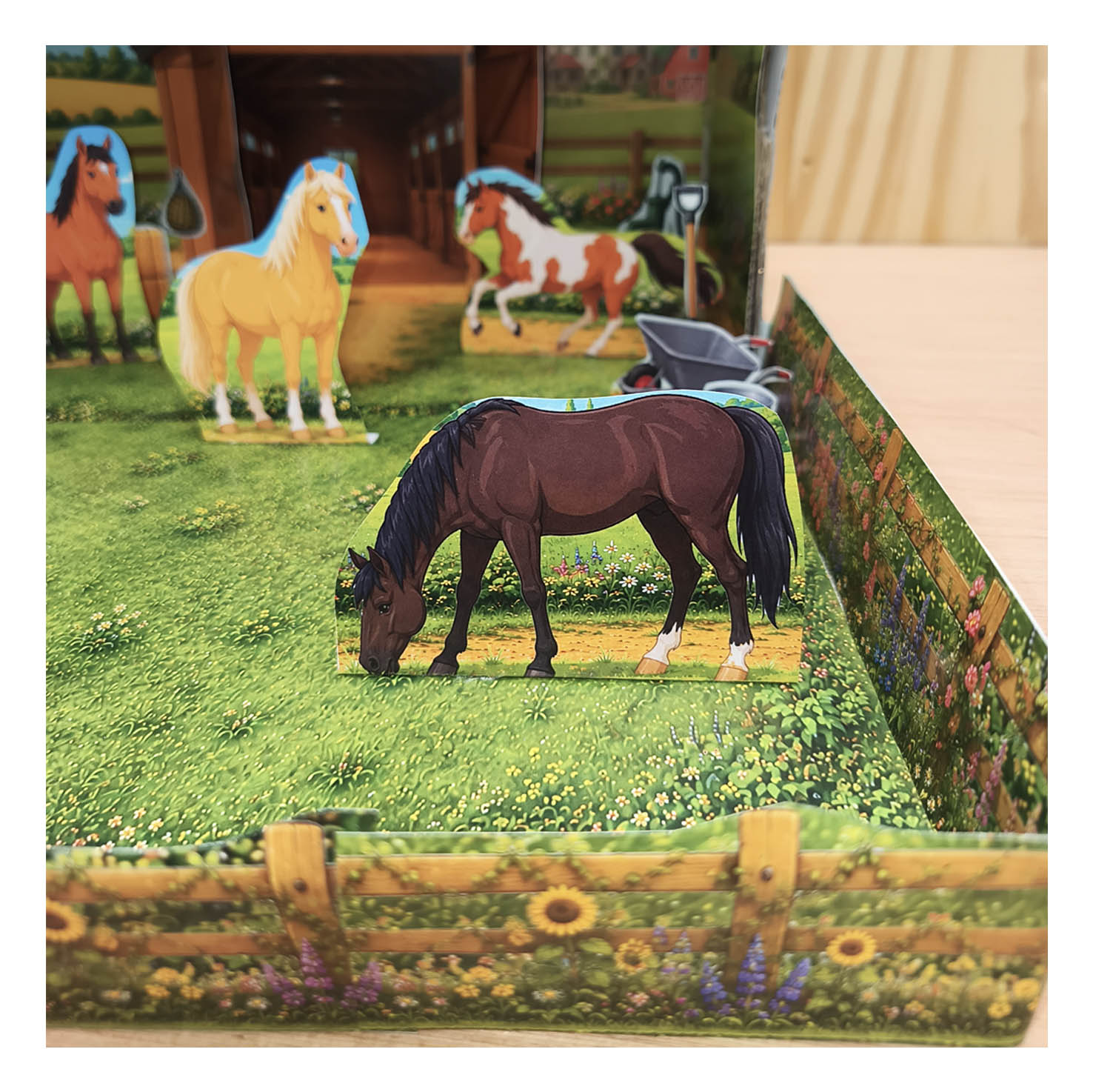 Paper horses standing in a grassy paddock with wooden flower fences and country scenery in a shoebox diorama