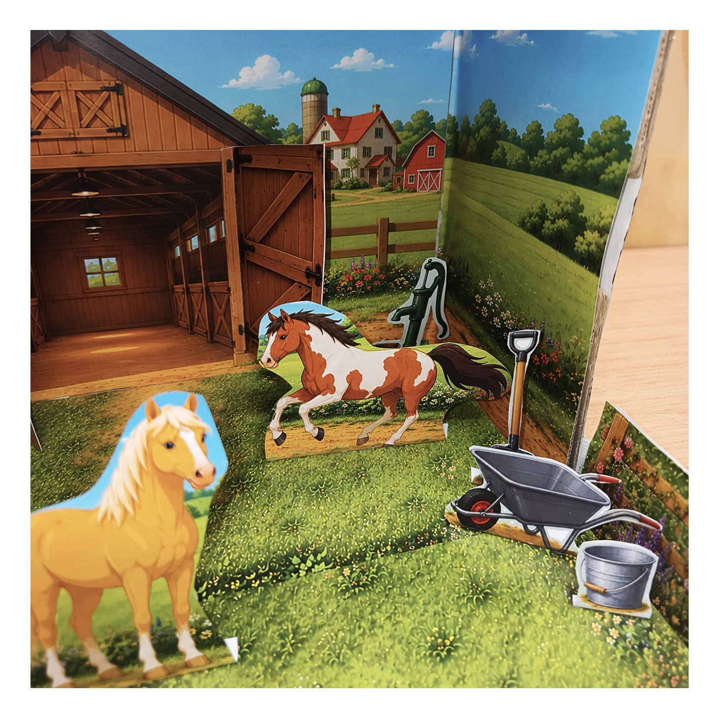 Close-up of the finished horse stable diorama with paper horses, flower-covered paddock fence and layered country background