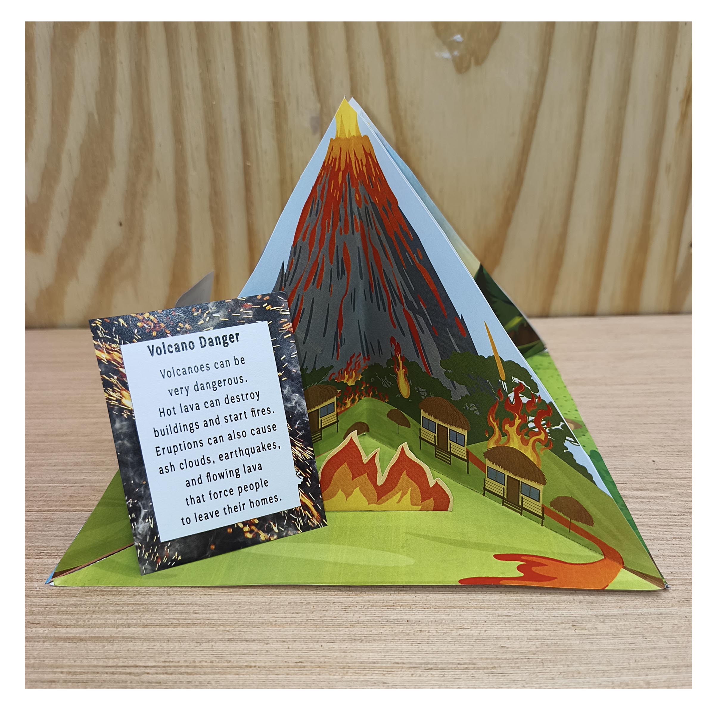 Volcano eruption hazards diorama with illustrated houses, lava, fire and an English information card