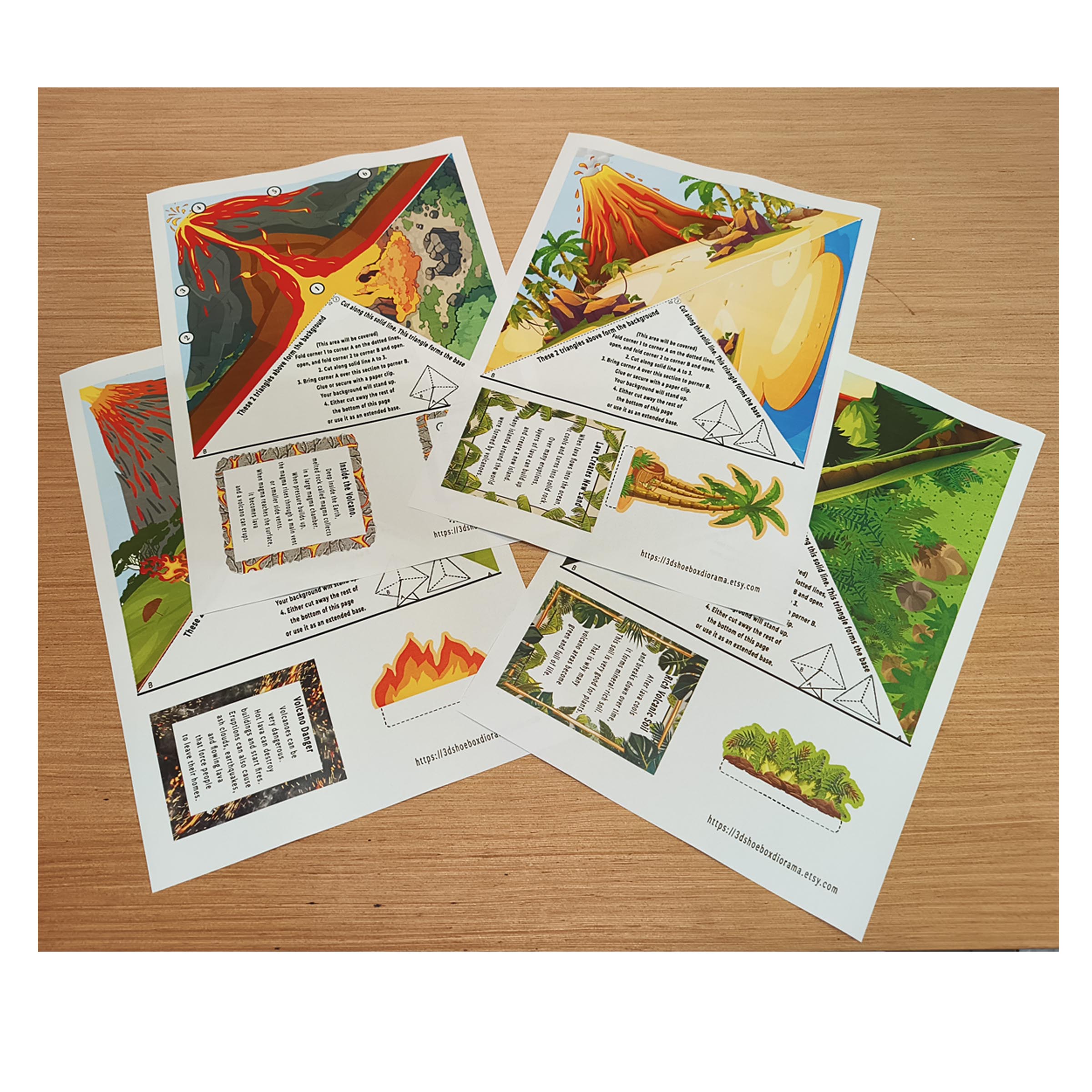 Four printed volcano model templates with scenery, folding instructions and educational cards on a wooden table